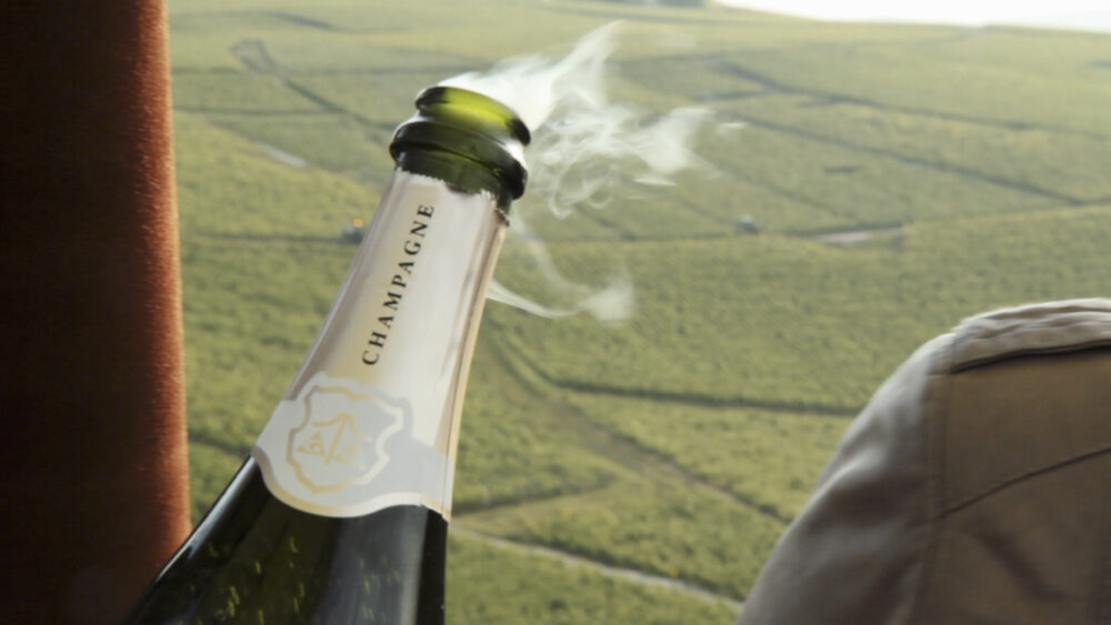 Champagne bottle with escaping bubbles, vineyards in background.