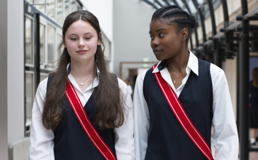 Two young women in school uniforms with red sashes, one looking at the other.