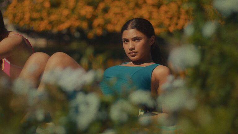 Woman in blue top relaxing outdoors near flowers, possibly related to "Short Films: Our Wealth in Common".