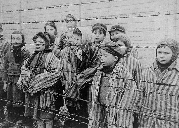 Children behind barbed wire at Auschwitz, wearing striped concentration camp uniforms.