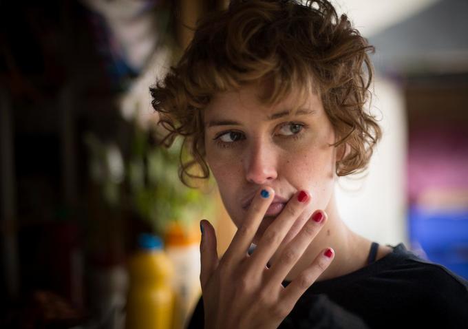 Woman with curly hair and colorful painted fingernails touches her face.