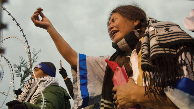 Woman protesting at Standing Rock, holding up a small object with emotion, wrapped in a blanket.