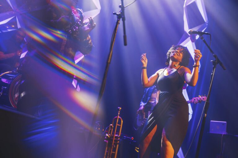 Singer performing on stage at the 2023 Opening Night Gala, with band and instruments in view.