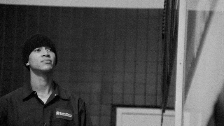 Black and white portrait of a person wearing a beanie and work shirt, looking up.