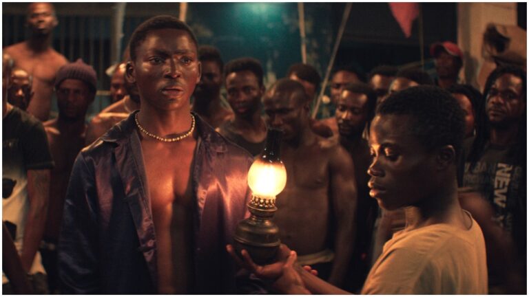 Scene from "Night of the Kings" movie: dark, intense, with men gathered around a lantern.