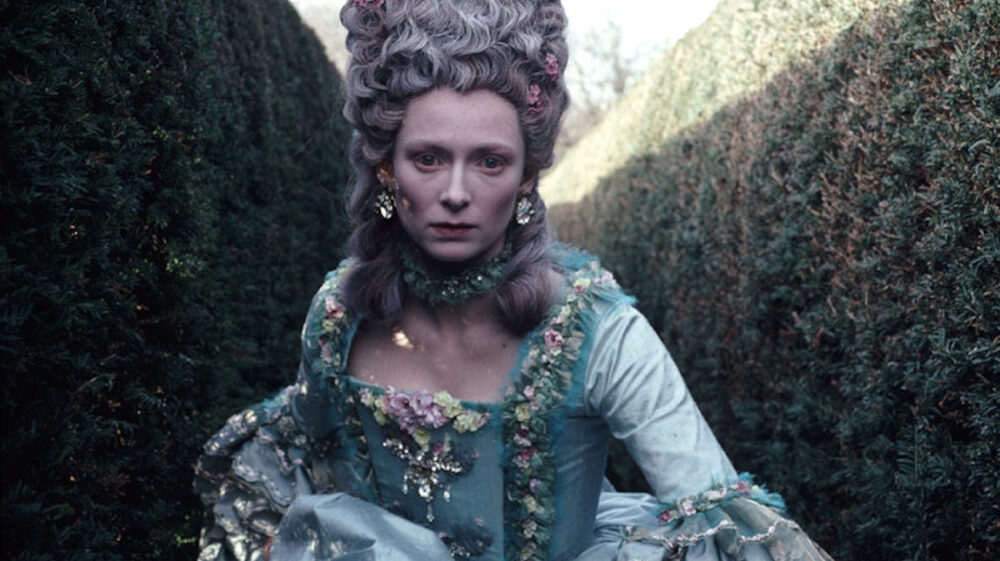 Tilda Swinton in Orlando costume: 18th-century style dress and powdered wig in a garden.