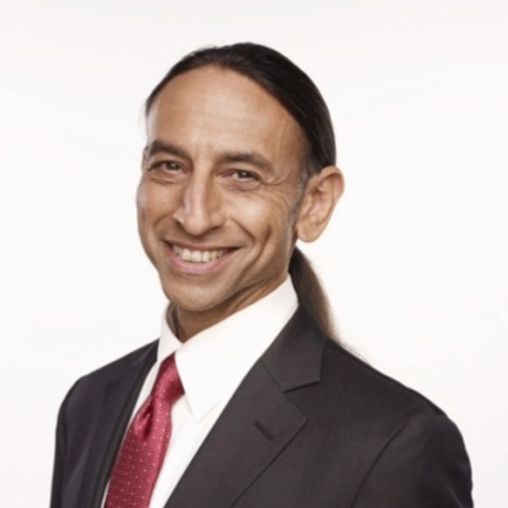 Scot Safon, smiling in a suit and tie with his hair in a ponytail.