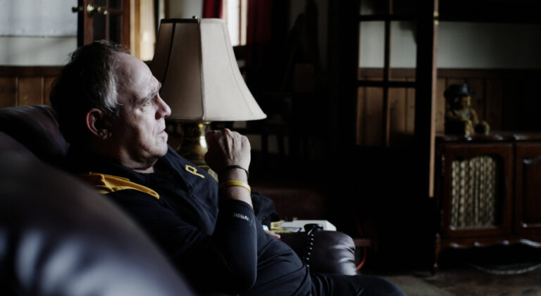 Man in black and yellow shirt sits contemplatively on a leather couch.