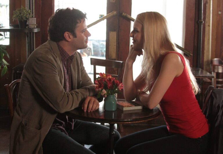Couple seated at cafe table with flowers, engaged in conversation.