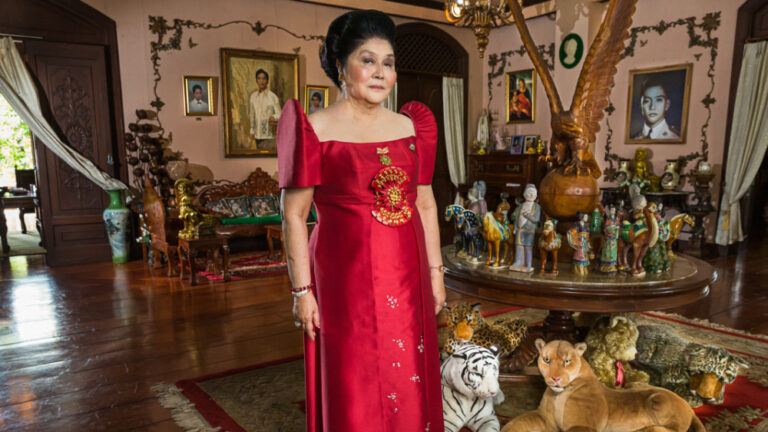 Imelda Marcos in red dress, surrounded by opulent decor.