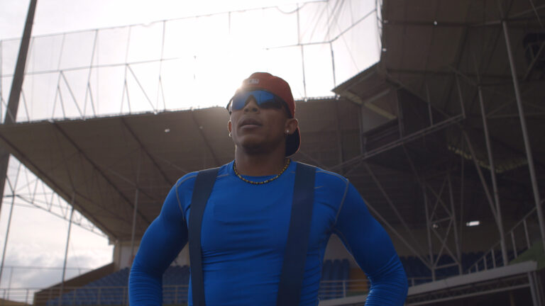 Baseball player in blue shirt and red cap stands in stadium.