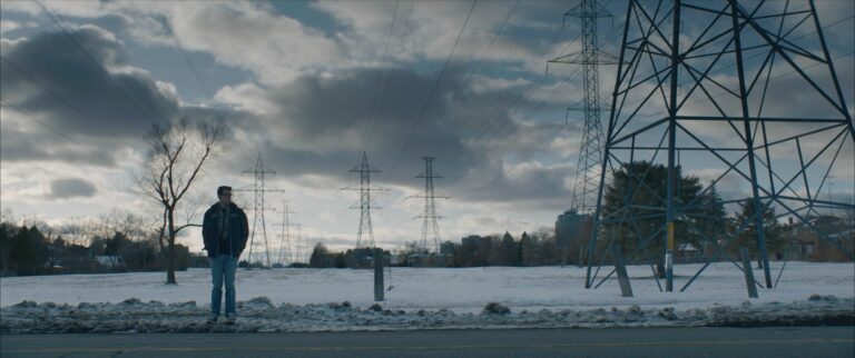 Man stands in snowy field under power lines, evoking "Demon Box" themes.