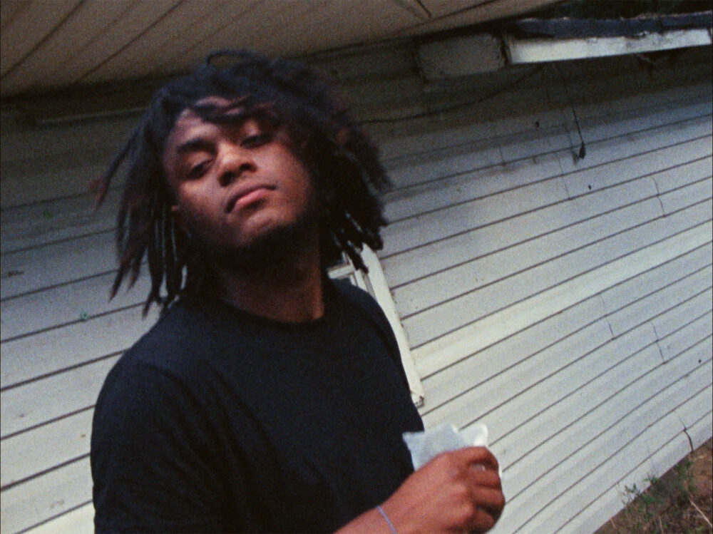 Kevin Jerome Everson in black shirt with dreadlocks, standing outdoors.