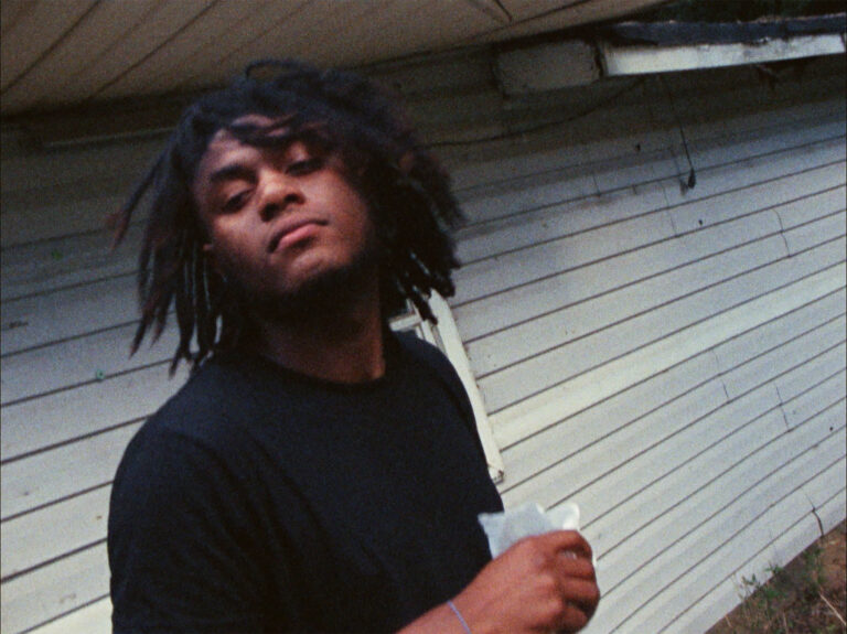 Kevin Jerome Everson in black shirt with dreadlocks, standing outdoors.