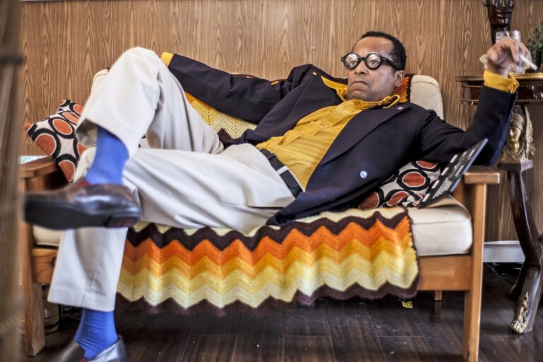 Man in vintage attire relaxing on a couch with a cigarette.