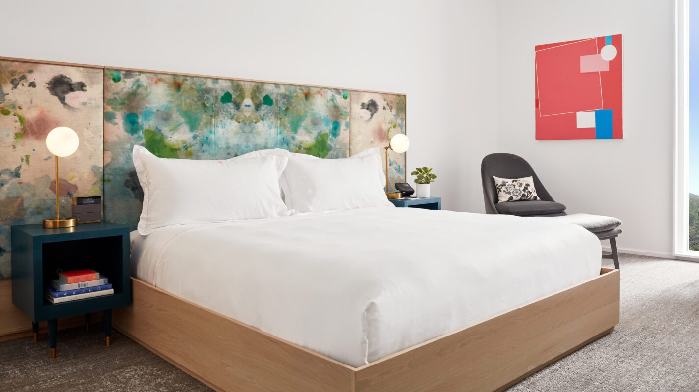 Modern hotel room with colorful headboard, white linens, and artistic decor. Travel &amp; Lodging.