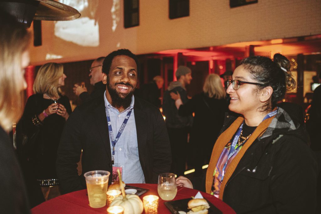 People at NEA 2023 event chatting around a table with drinks.