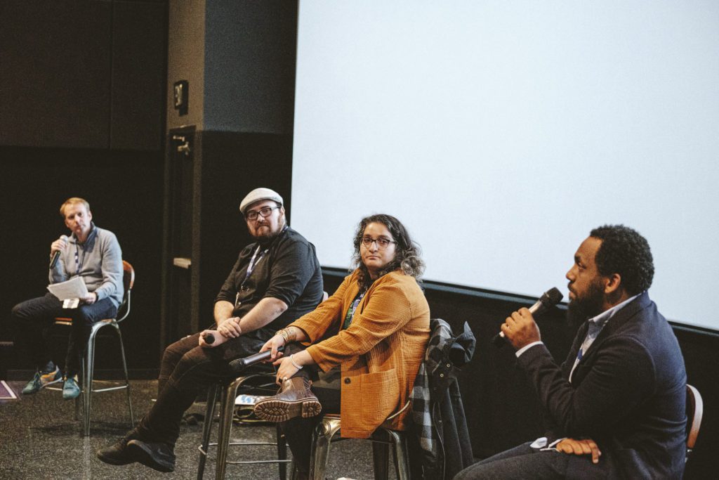 Panel discussion with four speakers on stools in front of a blank screen for NEA 2023.