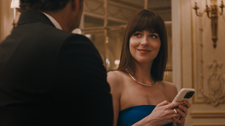 Dakota Johnson in a blue dress holding a phone, smiling at a man in a suit.
