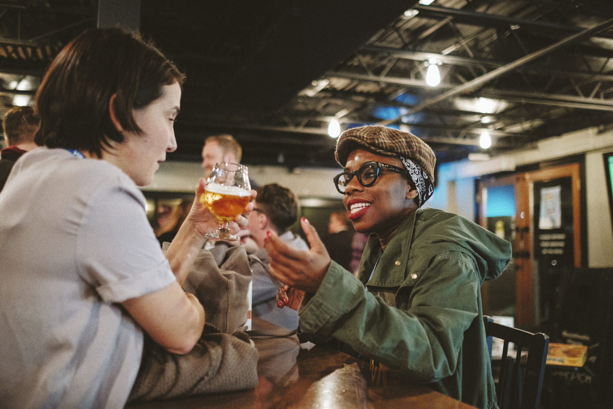 Two people at a bar, one holding a beer, engaging in conversation.