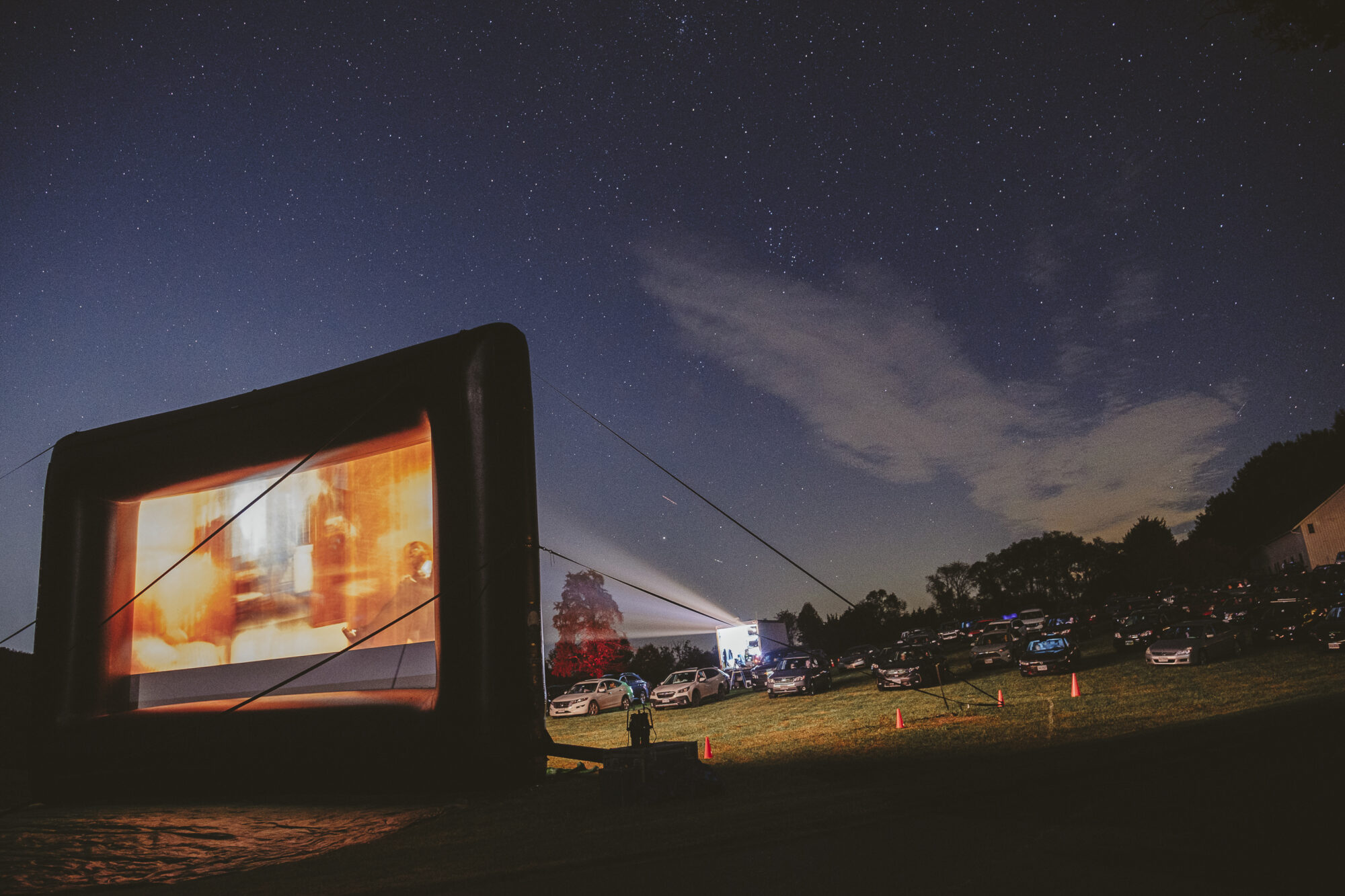 Drive-in movie night with cars parked under a starry sky, screen showing a film.