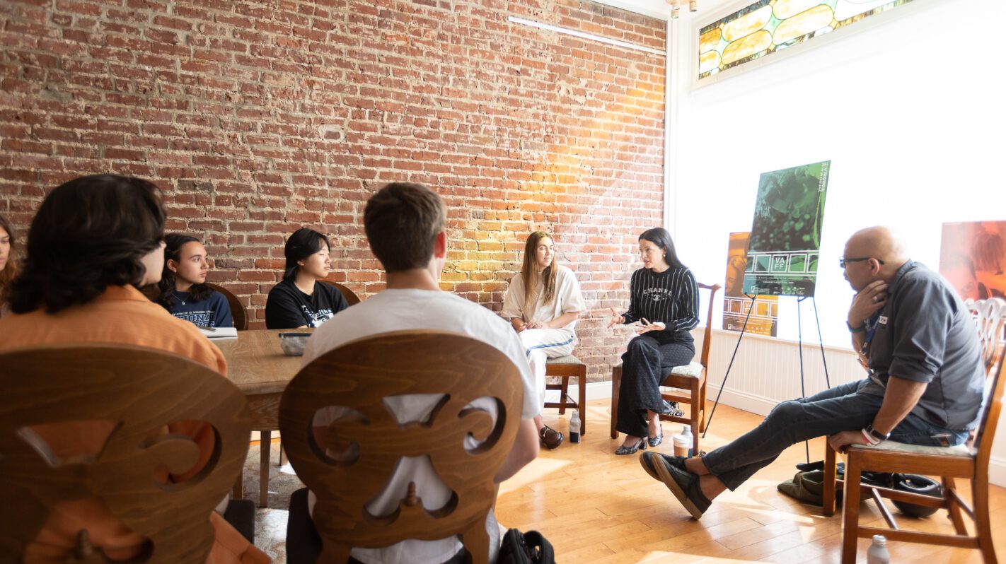 Group meeting in a room with a brick wall, featuring a diverse group of people.