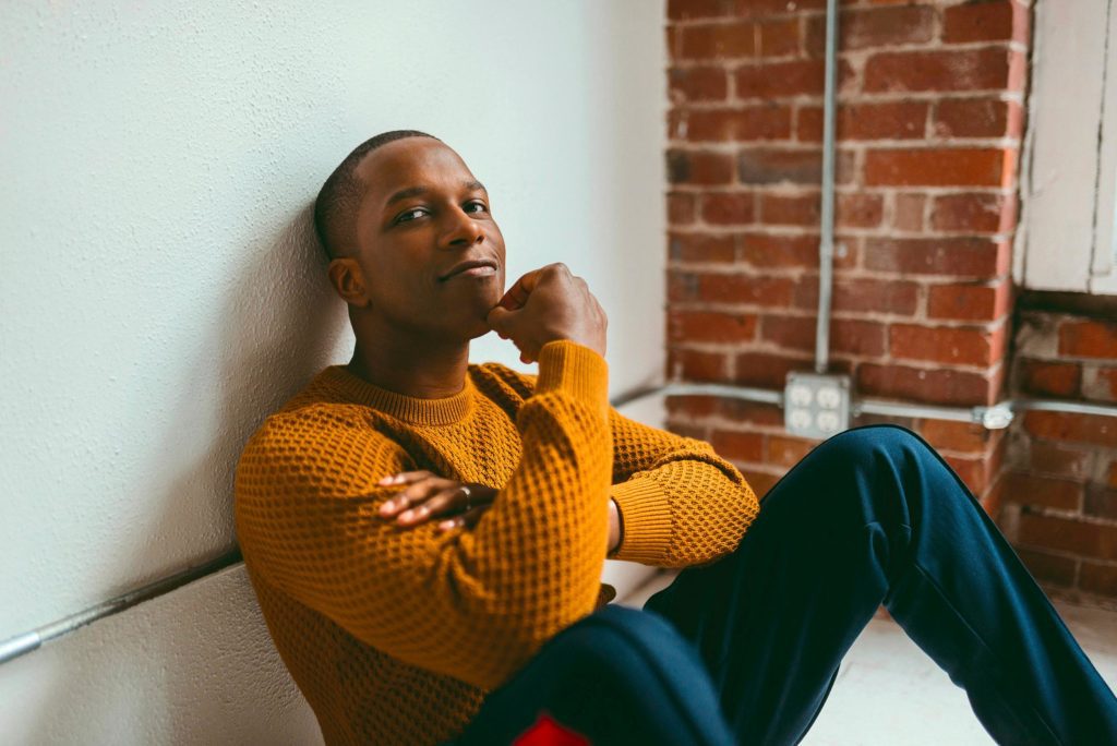 Man in mustard sweater leans against wall. NEA 2022 blog image.