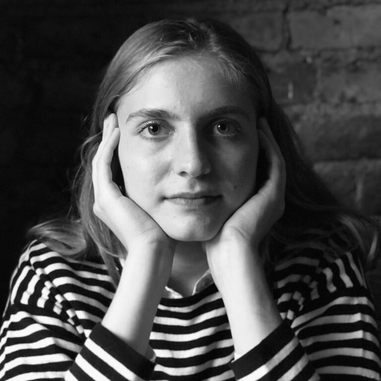Black and white portrait of Elizabeth Crowl wearing a striped shirt, hands on face.