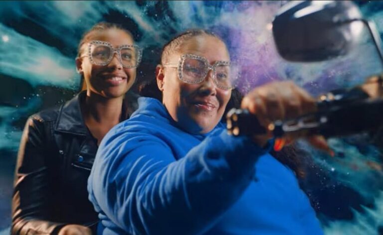 Two women wearing glasses on a motorcycle with galaxy background.