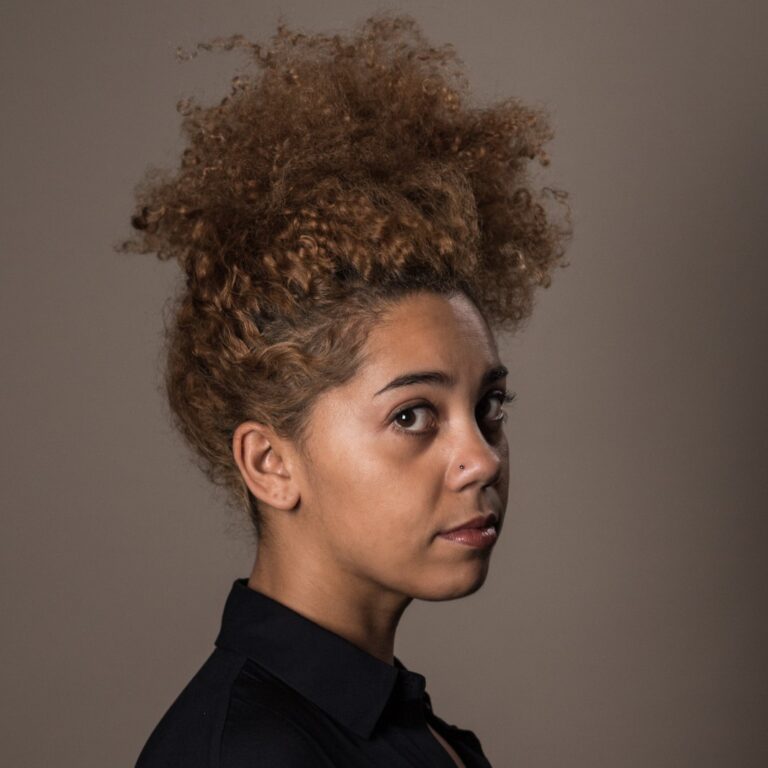 Melody C. Roscher with curly hair in a stylish updo, looking at the camera.