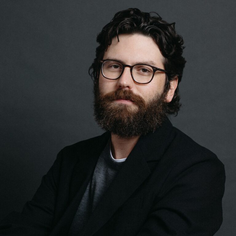 Morgan Evans portrait: Man with beard and glasses in black blazer.