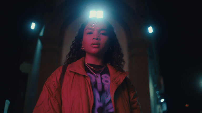 Woman in a jacket at night, under streetlights.