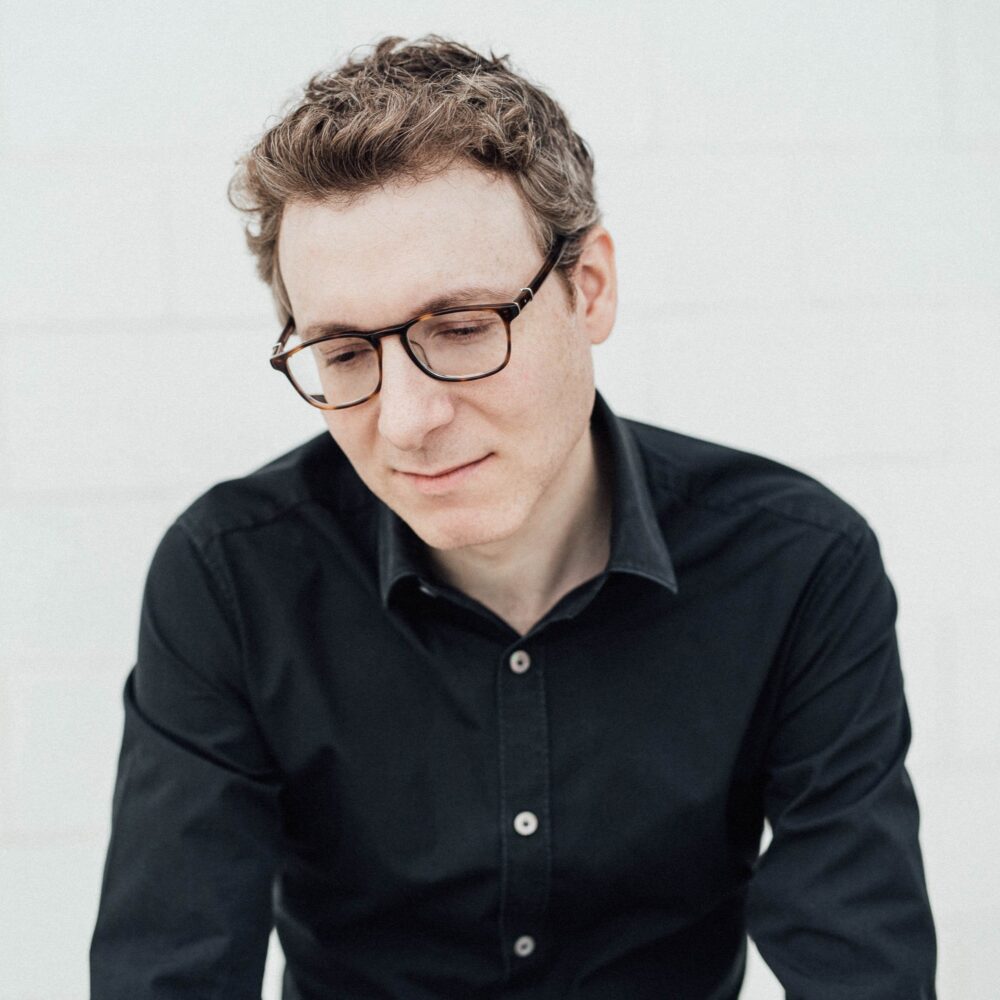 Nicholas Britell, portrait of the composer wearing glasses and a black shirt.