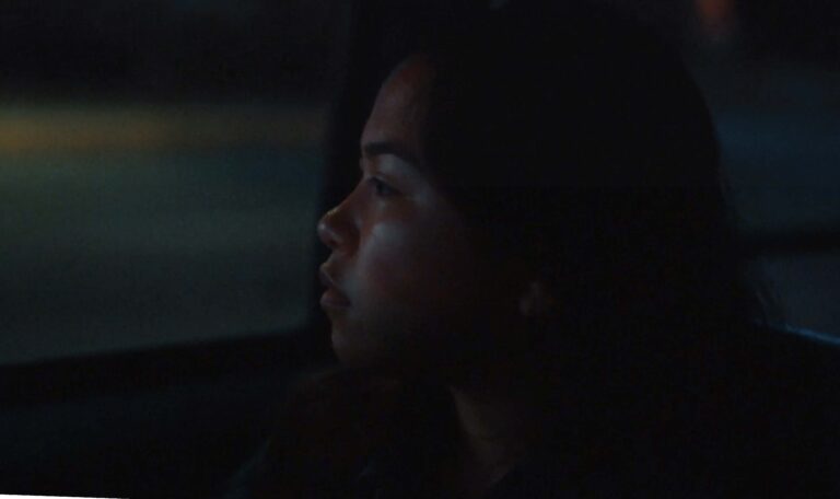 Film Still of young woman starting out of a car window at night.