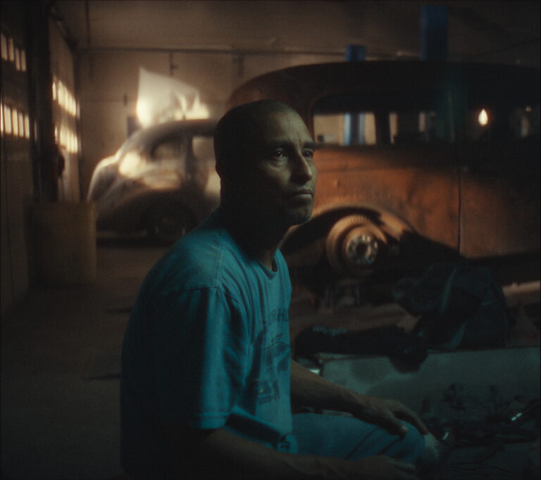 Man in garage with classic rat rod car.