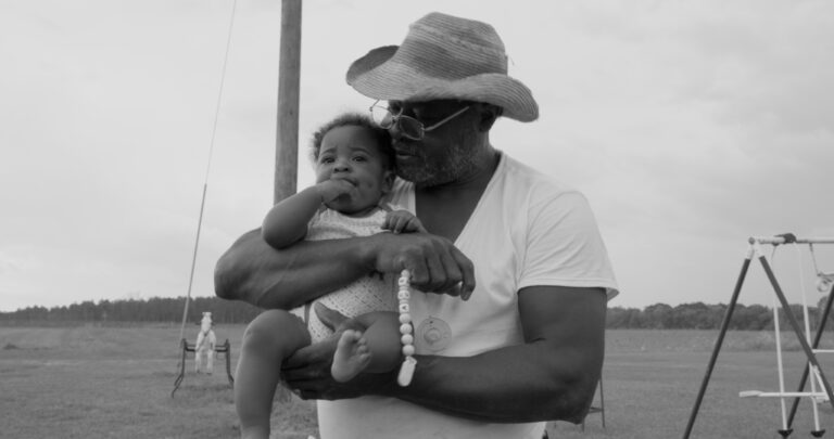 Grandfather holding baby in field, nurturing new seeds.