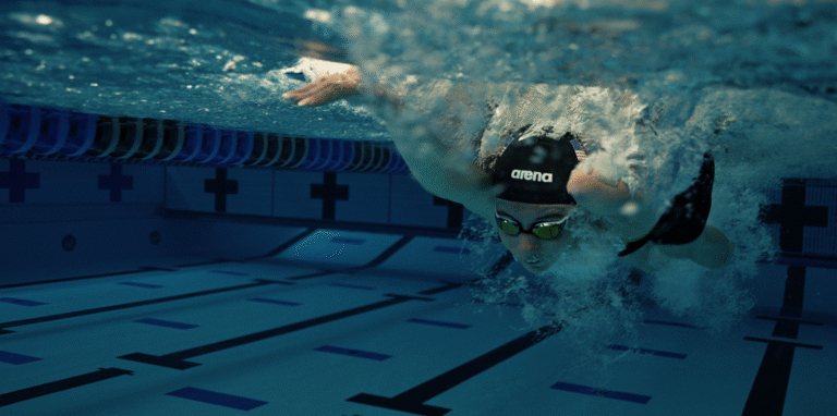 Swimmer underwater in pool, wearing Arena cap and goggles. Focus on butterfly stroke.