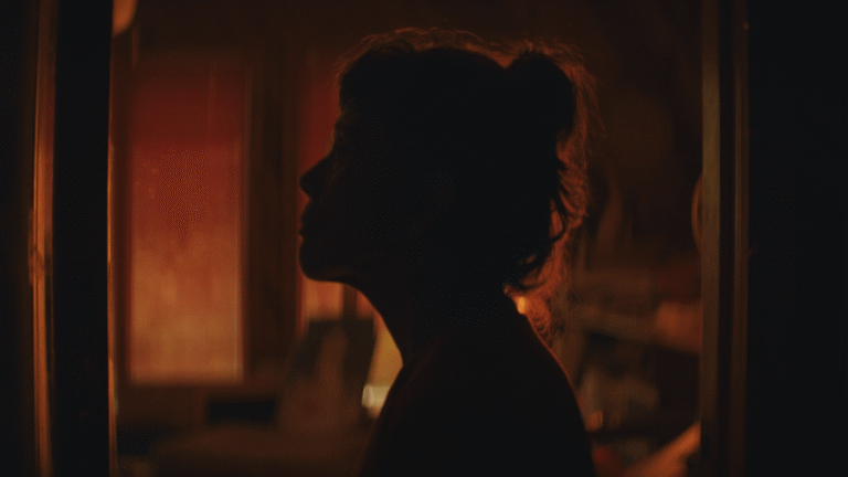 Silhouette of a woman looking out a window, bathed in warm, orange light.