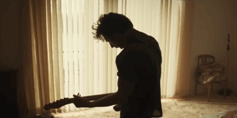 Silhouette of a man playing guitar in a sunlit room. Film still from DELIVER ME FROM NOWHERE